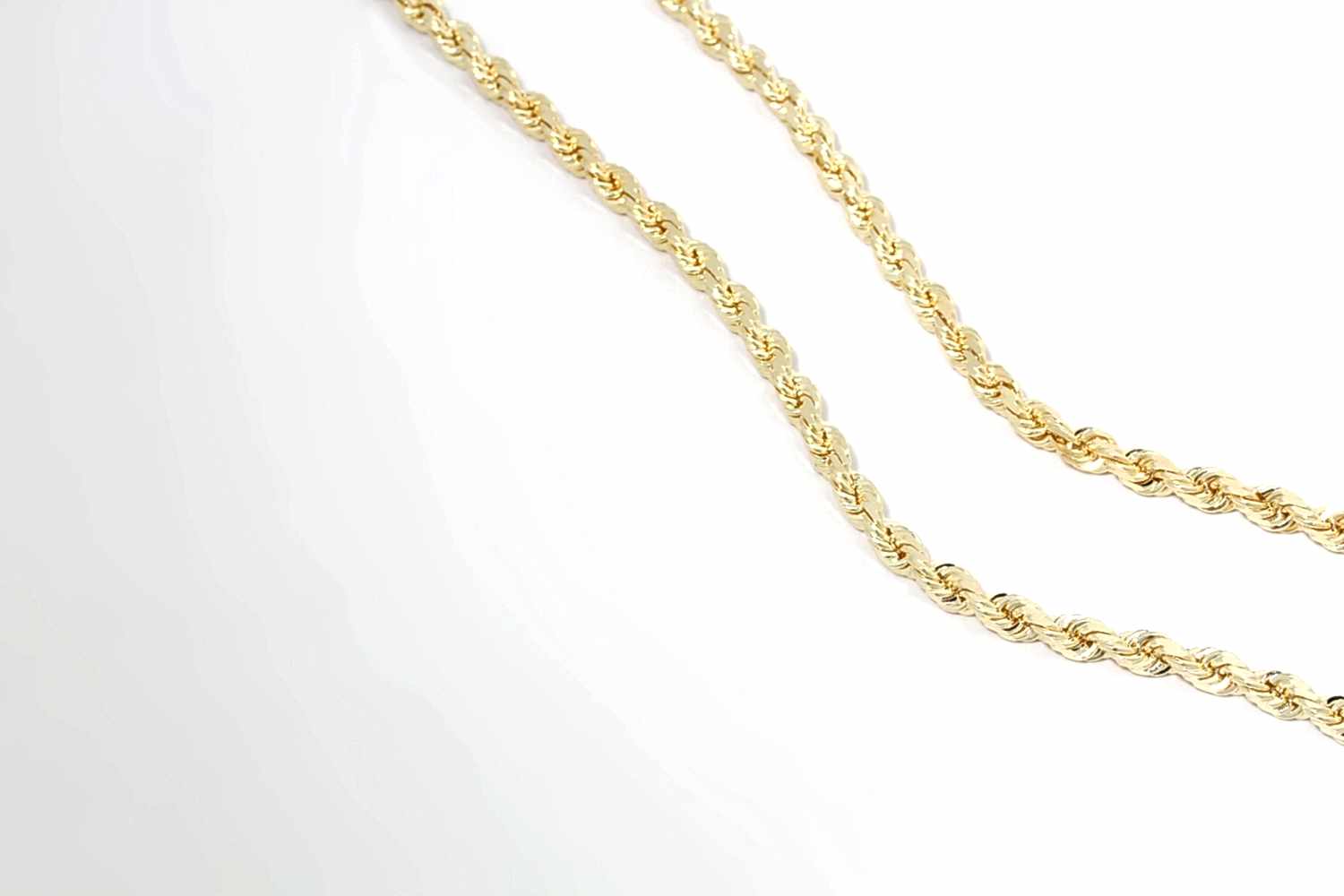 Two gold rope chains on display above a white backdrop. They are thin and intricate.