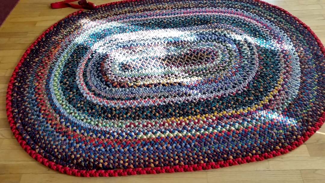 A multicoloured traditional wool braided rug is laying in a sunny spot on a hard wood floor.