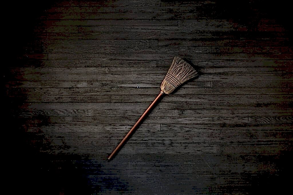 A broom is laying on a dark wood floor.