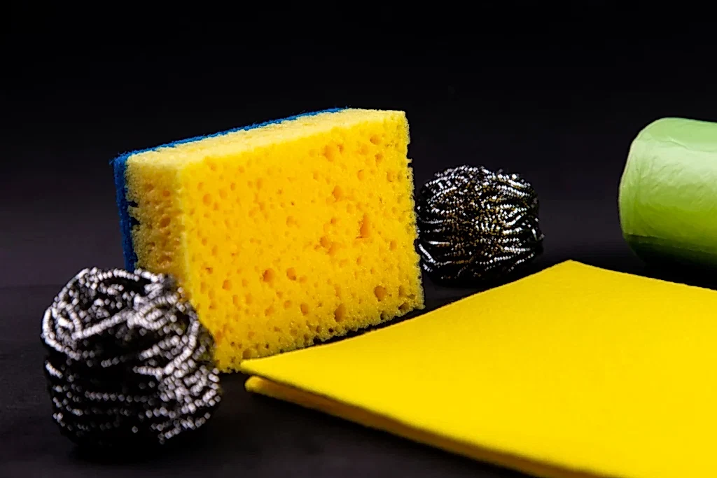 An array of sponges and scrubbers on a black background. You don't need to supply tools like this when hiring cleaners before move in.