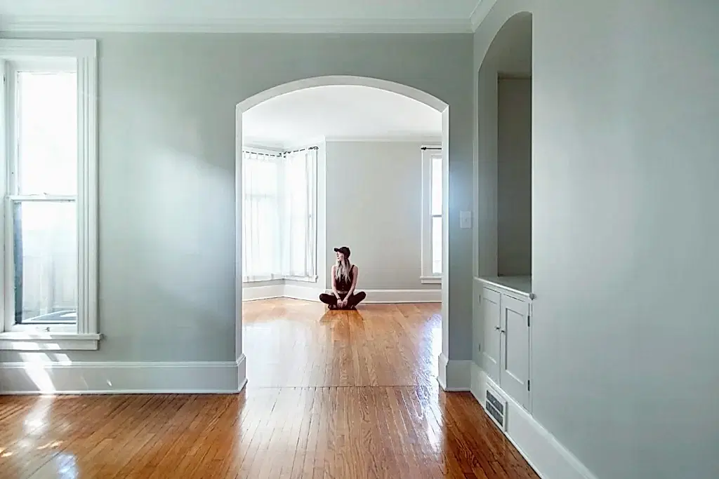 Someone is sitting in their empty home, after timing how long does a move out cleaning service take. The walls are clean and white, possibly freshly painted.