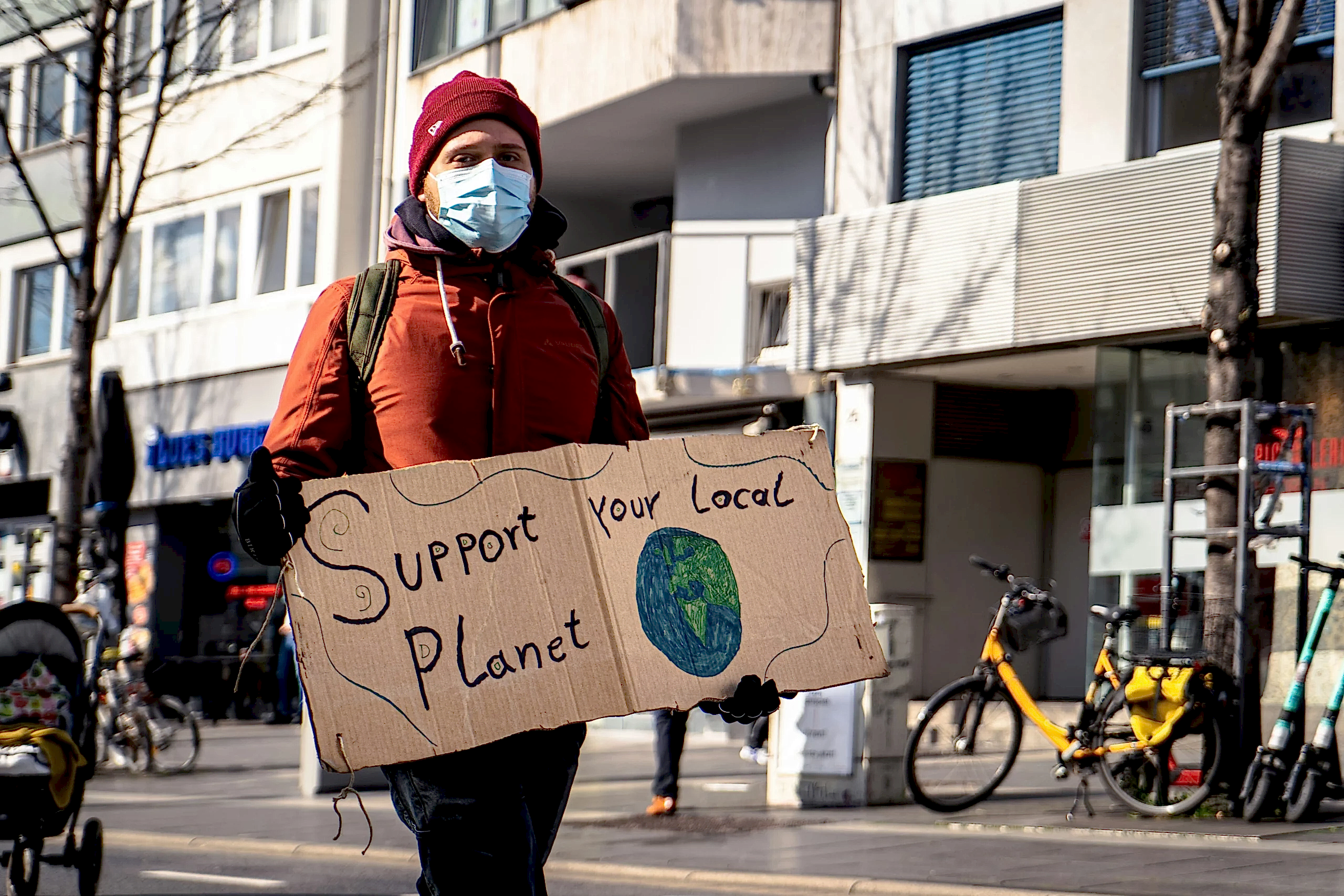 A man is holding a sign that says 'support your local planet'. He wants more people to use green cleaners and go green with eco friendly cleaning solutions.