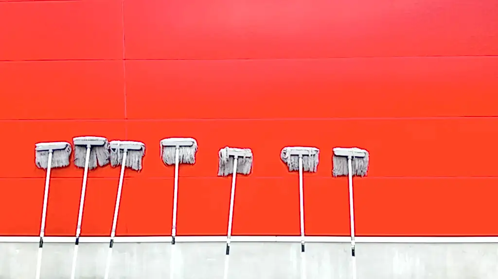 White mops left dripping against a red brick wall to dry. Whether you get deep cleaning vs move out cleaning, mopping is essential.