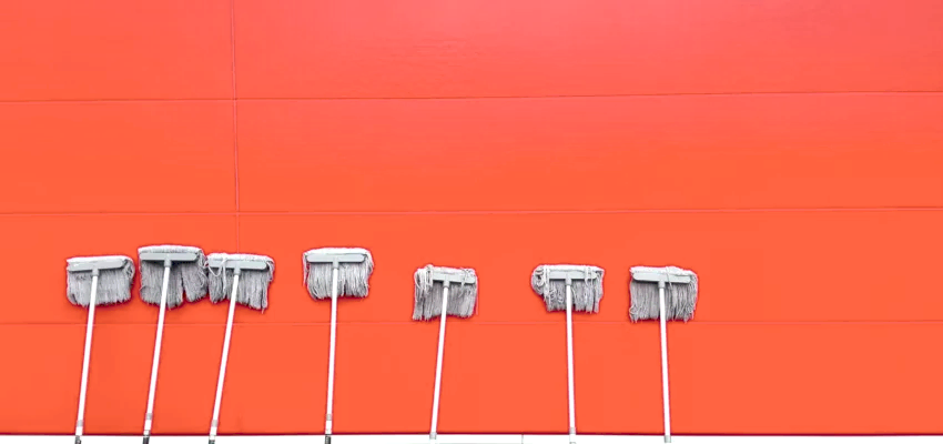 White mops left dripping against a red brick wall to dry. Whether you get deep cleaning vs move out cleaning, mopping is essential.