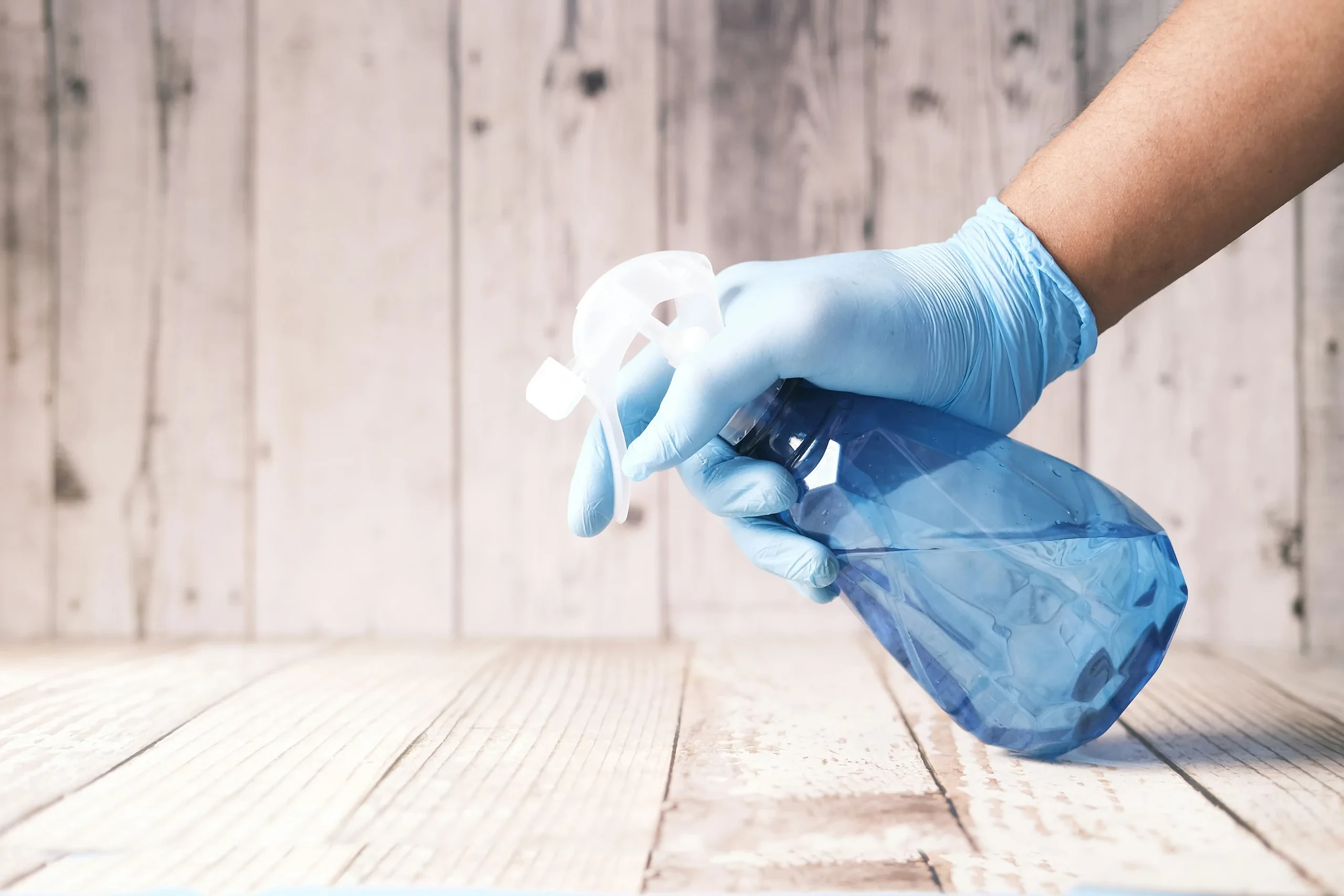 A spray bottle is being held towards a wooden surface. The solution is clear. They are using a green cleaner or eco friendly cleaning solution to clean the natural wood product.